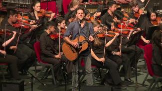 Lior playing a guitar in front of an orchestra at In Concert