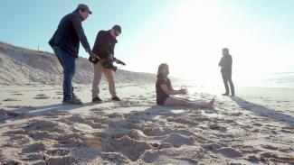 A film crew filming an actor sitting on a beach for the film Fight or Flight
