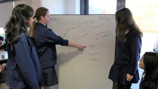 Three students looking at and pointing to a white board.