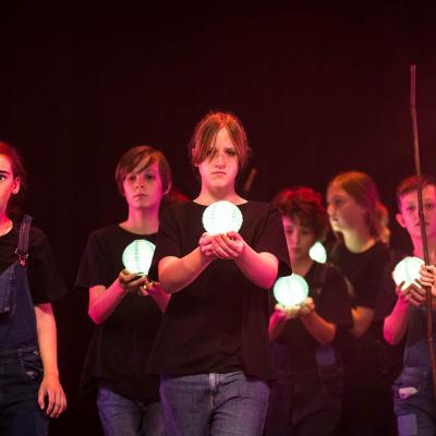 A group of students hold small round lanterns lit up in their hands with other students holding wooden rods stand either side